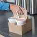 A hand holding a white Sabert drink carrier filled with cups of pink drinks.