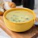 A yellow Libbey porcelain bouillon filled with soup on a white plate.