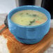 A blue Libbey porcelain bouillon filled with white liquid on a cutting board with a piece of bread.