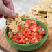 A hand holding a chip and dipping it into a bowl of salsa.