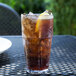 A GET clear plastic tumbler filled with brown liquid, ice, and lemon slices on a table.