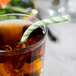 A glass of iced tea with a Creative Converting Fresh Lime and white striped straw in it.