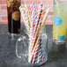 A glass jar filled with Creative Converting striped paper straws in assorted colors.