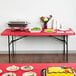 A red rectangular table with food on it and a yellow cake with balloons on it.