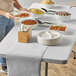 A woman serving food on a table with a Creative Converting silver glitter plastic table runner next to a bowl of food and stack of plates.