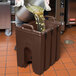 A man pouring liquid from a pot into a brown Cambro insulated soup container.