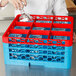 A person pouring water into a glass in a blue and red Carlisle glass rack.