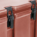 A close up of a brick red Cambro insulated soup carrier with black latches.