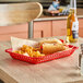 A red Tablecraft rectangular polypropylene fast food basket with hot dogs and fries on a table.