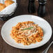 A Tuxton bright white china pasta bowl filled with spaghetti topped with cheese and rosemary on a table with bread.