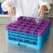 A chef using a Carlisle lavender color-coded glass rack with extenders to wash glasses in a dishwasher.