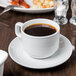 A Tuxton bright white china saucer with a cup of coffee on it.