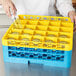 A person pouring water into a yellow Carlisle glass rack on a counter.