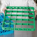 A person holding a green Carlisle glass rack extender on a green plastic tray.