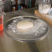 A dough ball on an American Metalcraft aluminum pizza pan on a surface.