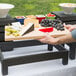 A hand holding a Vollrath cutting board with grapes and cheese on a table.