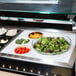 A white Cambro salad bowl holder on a counter with bowls of green and red lettuce, broccoli, and tomatoes.