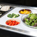 A Cambro salad bowl holder on a counter with bowls of broccoli, green and red lettuce, and tomatoes.