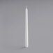 A Will & Baumer white taper candle on a gray surface.