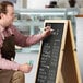 A man using a Choice A-Frame Marker Board on a table in a coffee shop.