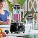 A commercial blender with a black base, toggle controls, and two clear 64 oz. containers, one filled with a purple smoothie.