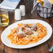 An oval ivory porcelain platter with a plate of pasta with meatballs and cheese on it.