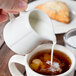 A person pouring cream into a cup of coffee.