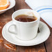 A Libbey porcelain saucer with a cup of tea and orange slices on a wooden table.