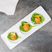 A Libbey porcelain 3-well tray with three small plates of food on a table.