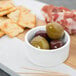 A Libbey ultra bright white porcelain bowl filled with green olives and crackers on a cutting board.