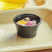 A black Choice plastic souffle cup filled with yellow liquid.