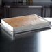 A rectangular white fiberglass MFG Tray sheet pan extender on a metal tray with brown substance inside.