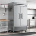 A large stainless steel True reach-in refrigerator with two solid doors in a kitchen.