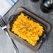 A Lodge rectangular wood underliner with macaroni and cheese on a table.