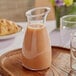 A Carlisle polycarbonate carafe of liquid on a wooden tray with a plate of food on a table in a brunch café.