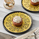 A gold foil lace doily under a chocolate cake with white frosting and sprinkles on a plate.