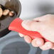 A hand using a red Lodge Mini Silicone handle holder on a pan.