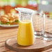 A Carlisle polycarbonate carafe filled with yellow liquid on a table with empty glasses.