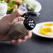 A person holding a Tablecraft glass salt shaker with a black top.