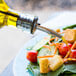 A Tablecraft olive oil cruet pouring oil on a salad on a table.