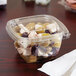 A plastic container with food in it on a table with olives and grapes.