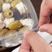 A person cutting green olives and green peppers into a Sabert clear plastic bowl.