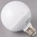 A Satco frosted warm white LED globe light bulb on a gray surface.