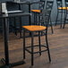 A Lancaster Table & Seating black cross back bar stool with a cherry wood seat on a table in a restaurant.