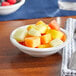 An Acopa bright white stoneware fruit bowl filled with berries on a blue table.