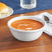 A white Acopa stoneware nappie bowl filled with brown soup on a table.