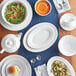 A close up of a white Acopa stoneware cup on a table with plates and bowls of food.