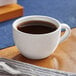 An Acopa bright white stoneware cup on a table with a spoon