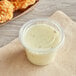 A plastic container of white sauce with a Choice PET plastic lid next to fried chicken.