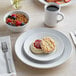 A white Acopa stoneware plate with a bowl of cereal, berries, and a biscuit with jam on it.